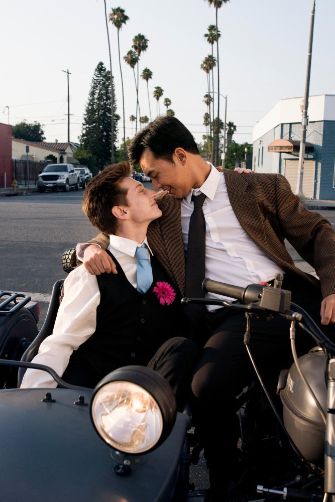 Two grooms smiling at each other in a car on their wedding day.