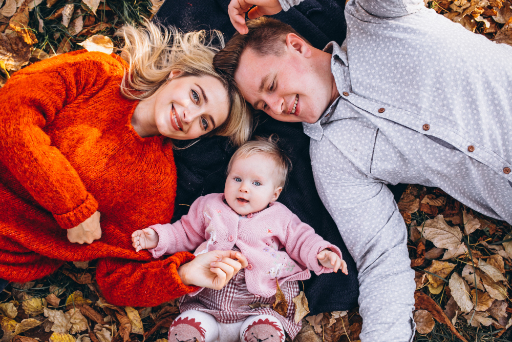 Mum, dad, and their baby lying on leaves and looking up at the camera.
